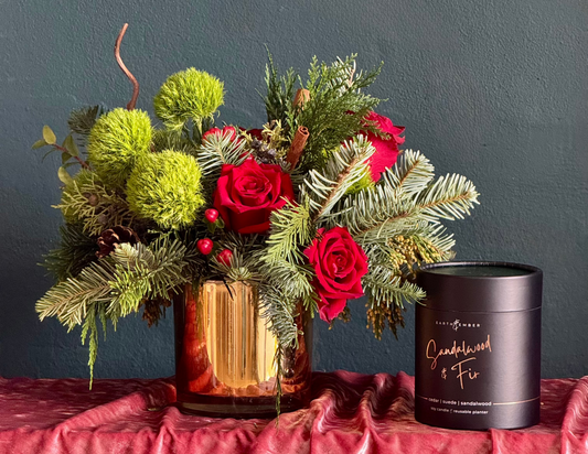 gold base green ball flower, red roses  and evergreens and a black round box with a sandalwood and fir candle