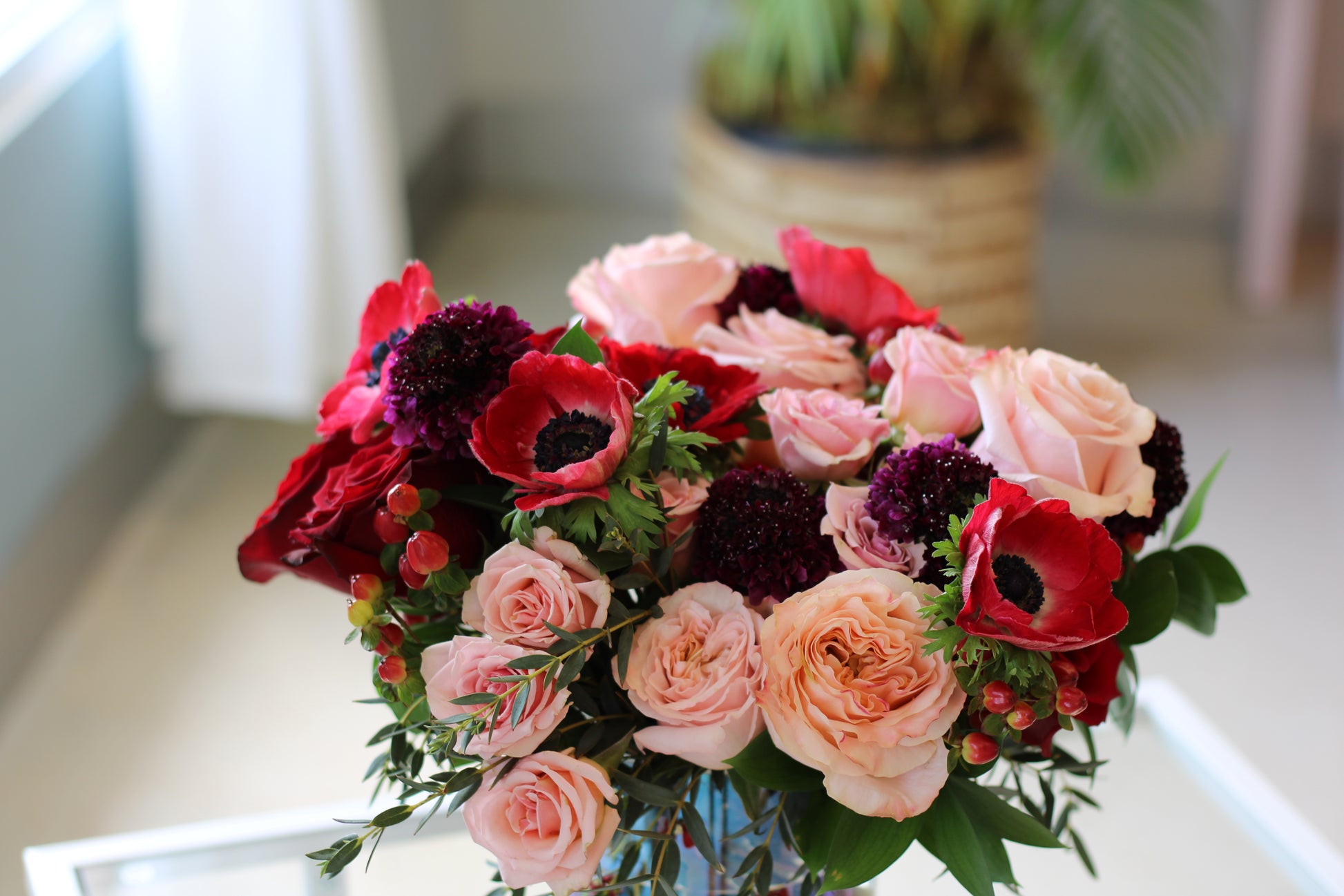 red anemones, shimmer rose and explorer rose with fillers in clear vase 